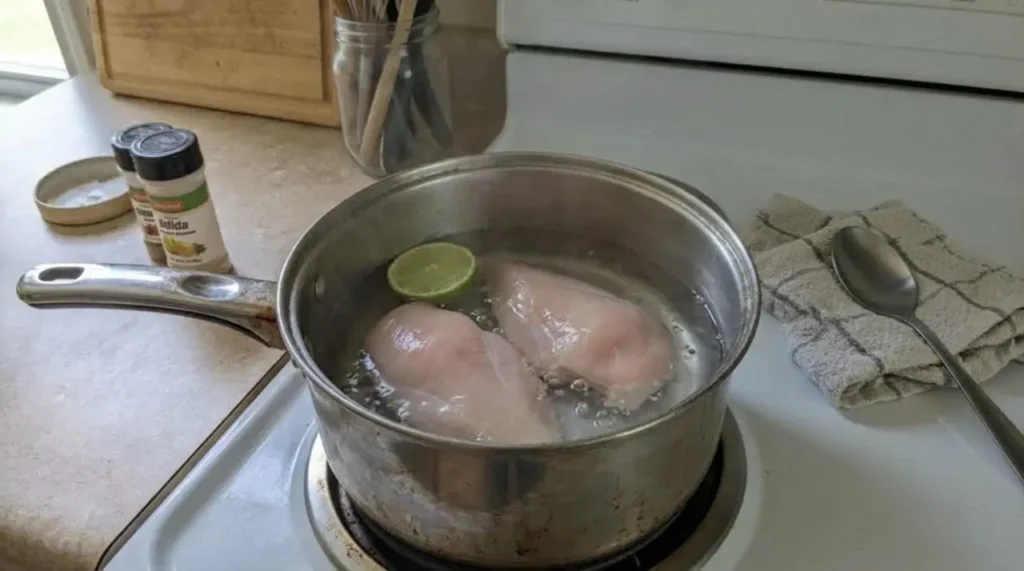 Chicken breasts gently poaching in a pot with a few lime halves nearby