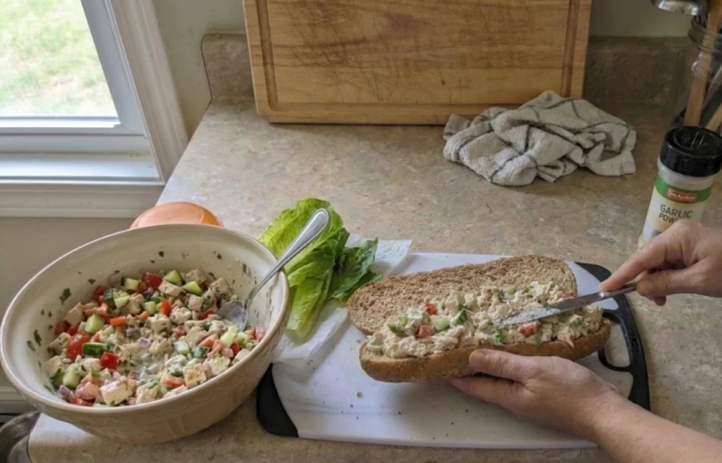 Chicken salad being spread over lettuce on soft brown bread